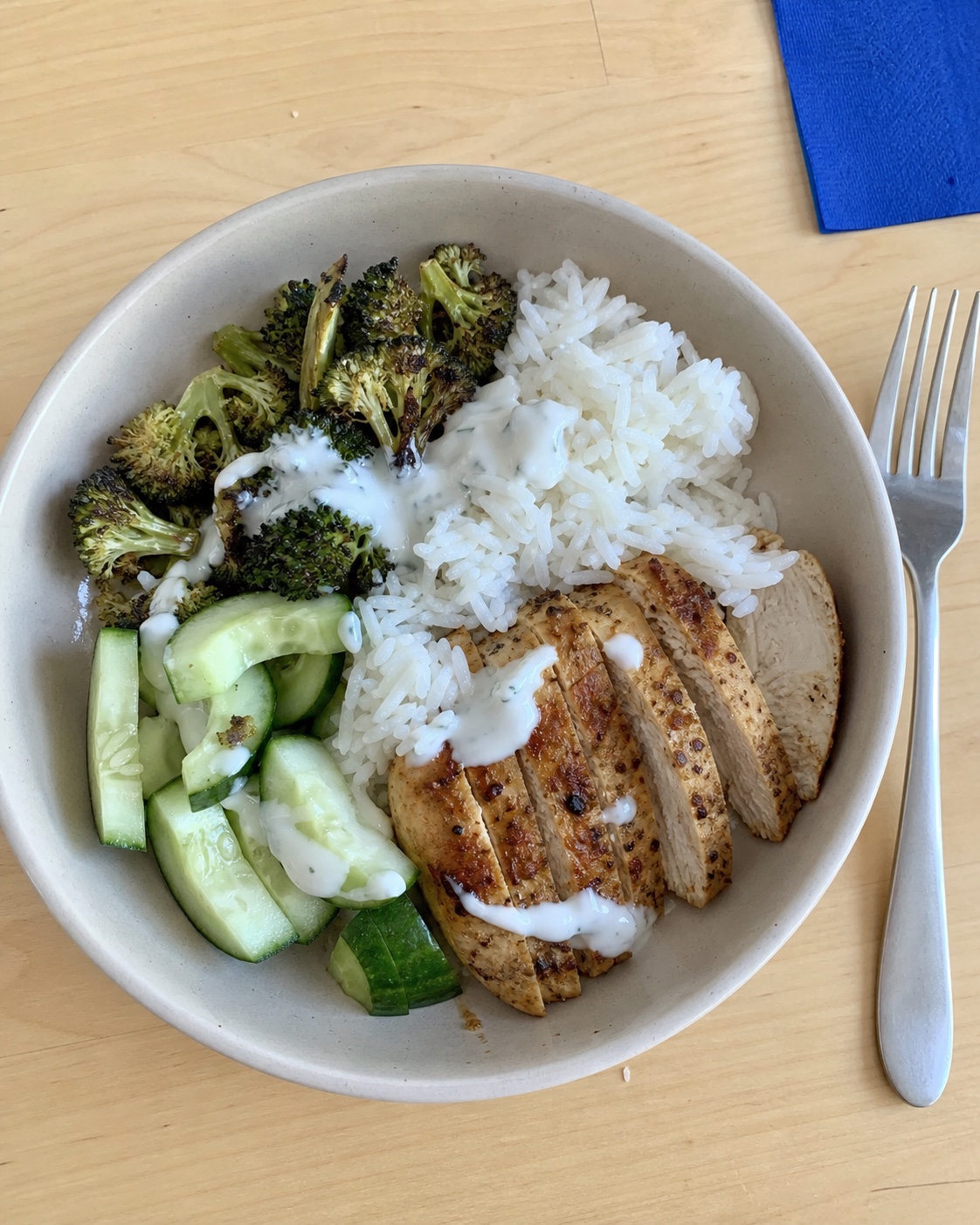 Top-down photo of a chicken, rice, broccoli, and cucumber lunch bowl